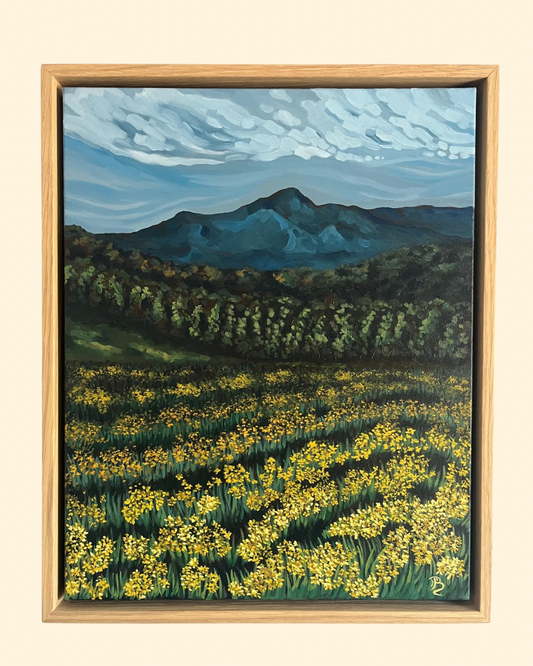 Original oil painting of a mountain range and forest tree line in the background with a meadow of yellow wildflowers in the foreground.
