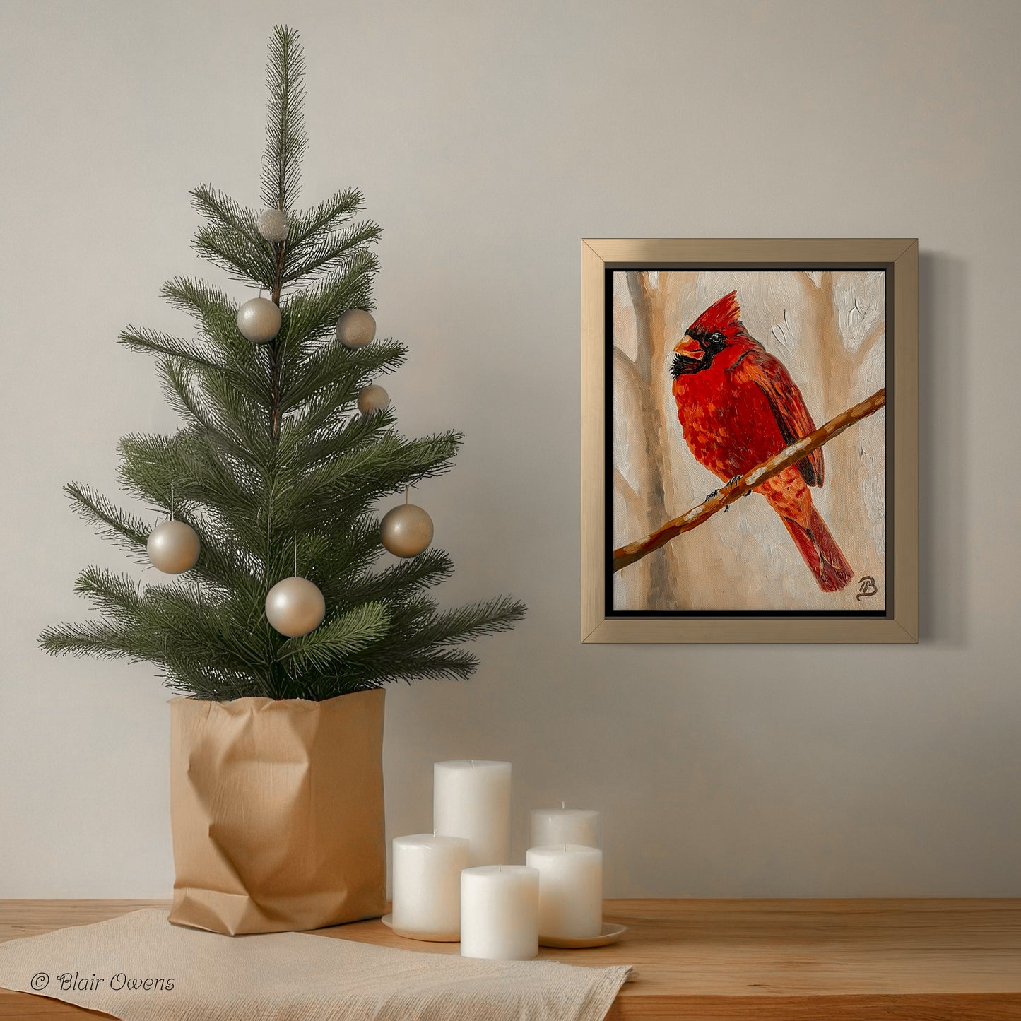 Decorative setup with a small Christmas tree, candles, and a framed painting of a red cardinal on a wall.