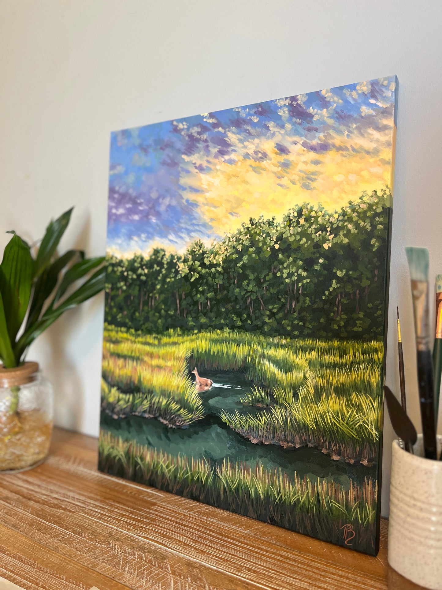 Landscape painting of a marsh at sunset with a deer wading through the water and grasses.