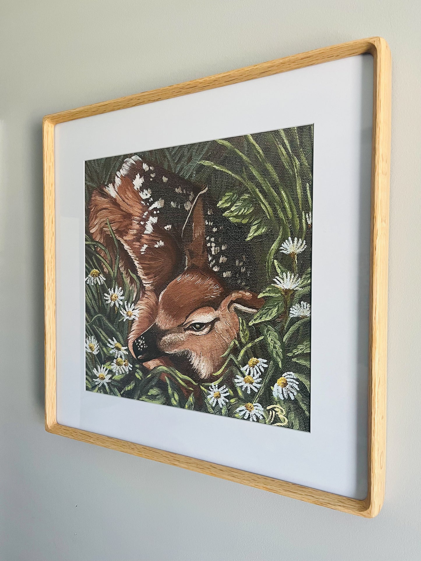 Framed artwork of a deer in a meadow hung on a wall.