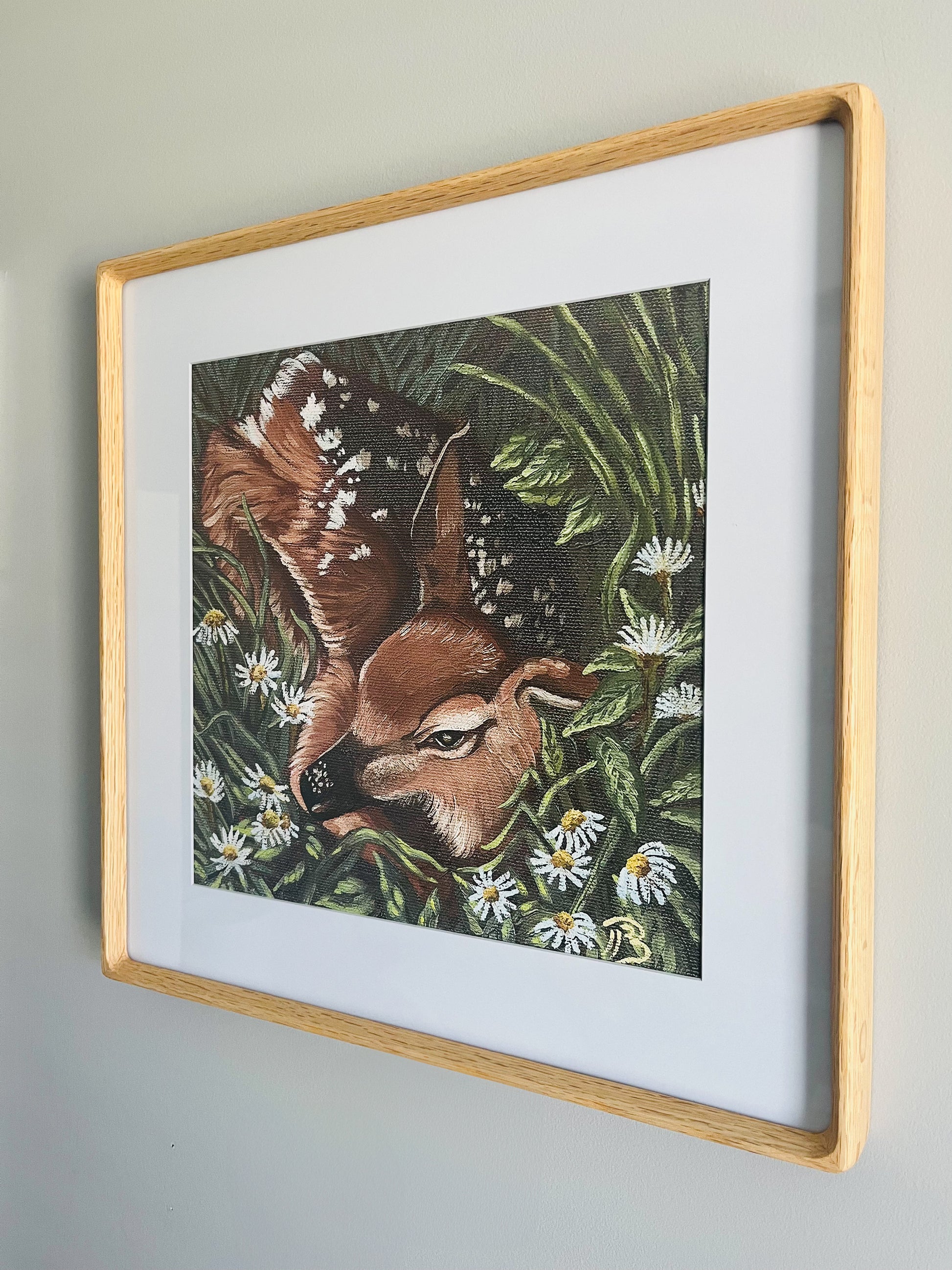 Framed artwork of a deer in a meadow hung on a wall.