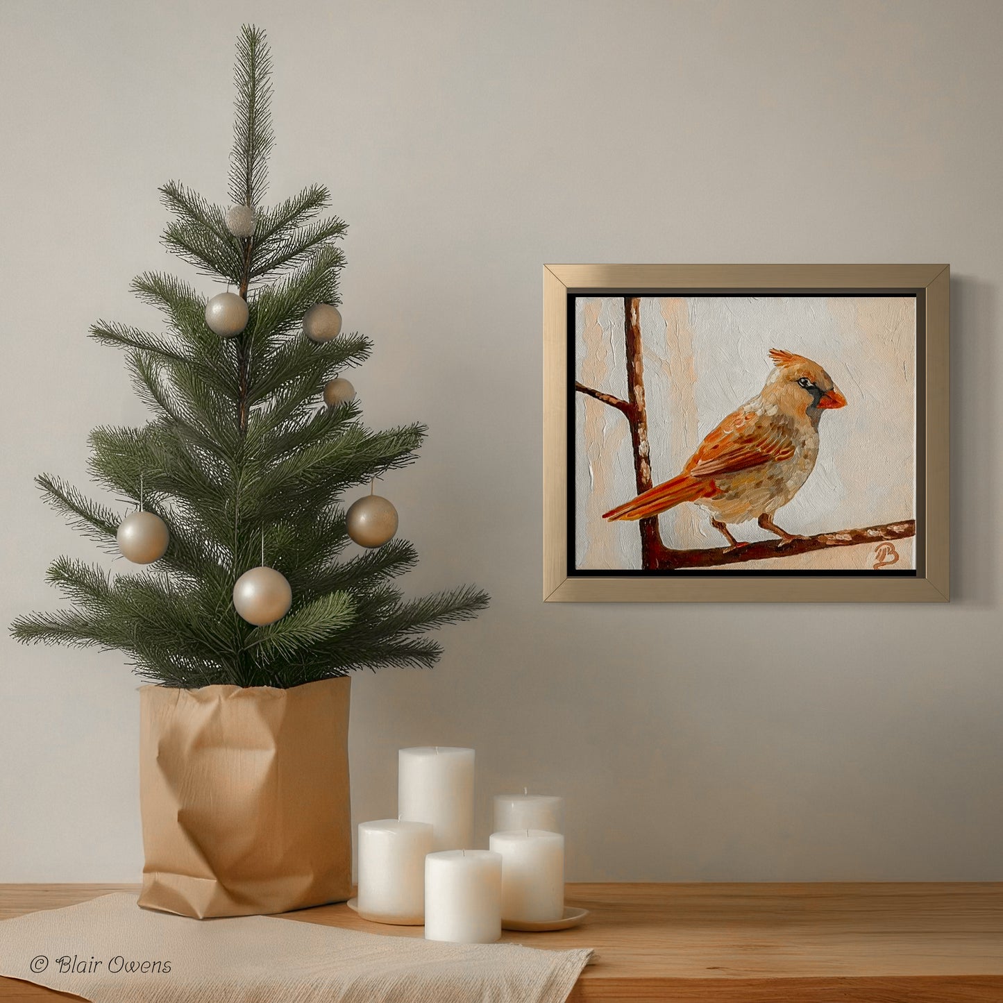 Decorative setup with a small Christmas tree, candles, and a framed painting of a female cardinal on a wall.