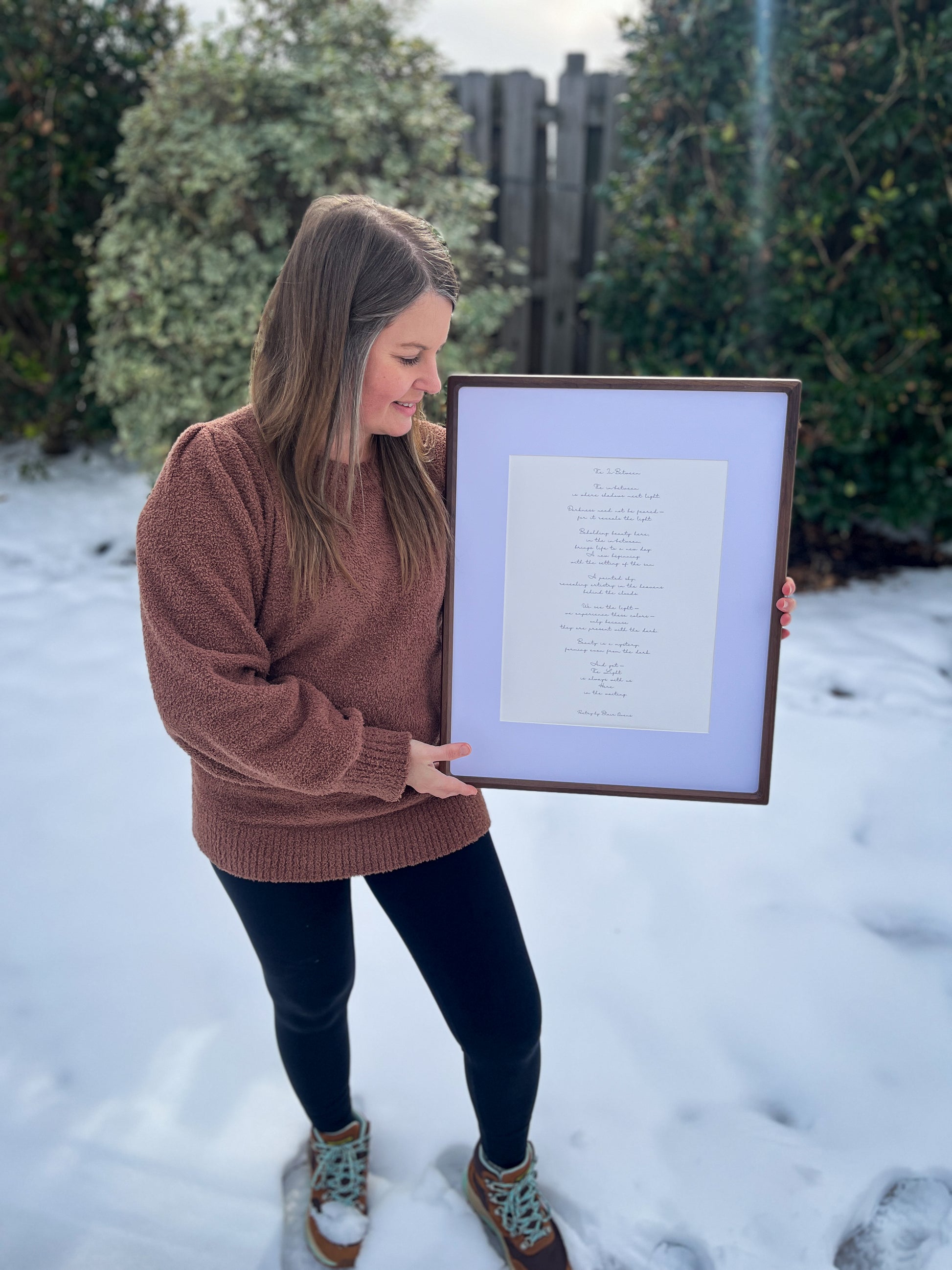 Artist, Blair Owens, holding a framed poem in a snowy outdoor setting