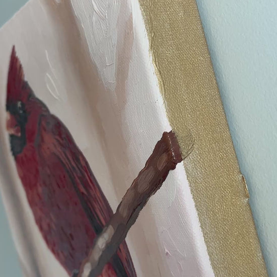 Video close-up of red cardinal painting with gold painted canvas edges.